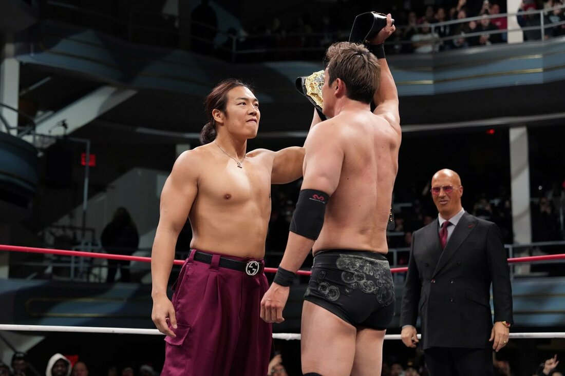 ベルトを掲げ、オカダ(右)とにらみ合う竹下幸之介(©All Elite Wrestling)