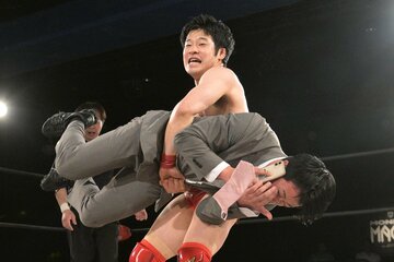電話中の新橋二郎（手前）を抱えあげる小田嶋大樹
