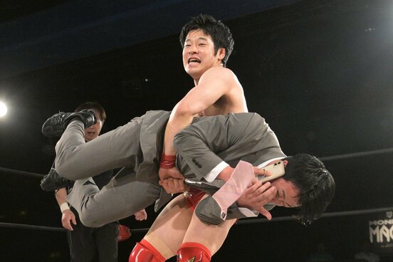 電話中の新橋二郎(手前)を抱えあげる小田嶋大樹