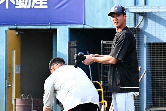 居残り特打中に「師匠」山川穂高の背中をマッサージ機でほぐしつつ、カメラ目線のソフトバンク・秋広優人