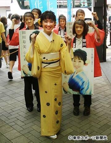 田川のお面をつけた女性スタッフと田川寿美（中央）