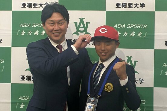 1位指名の亜大・山里(右)に帽子を被せる新井監督