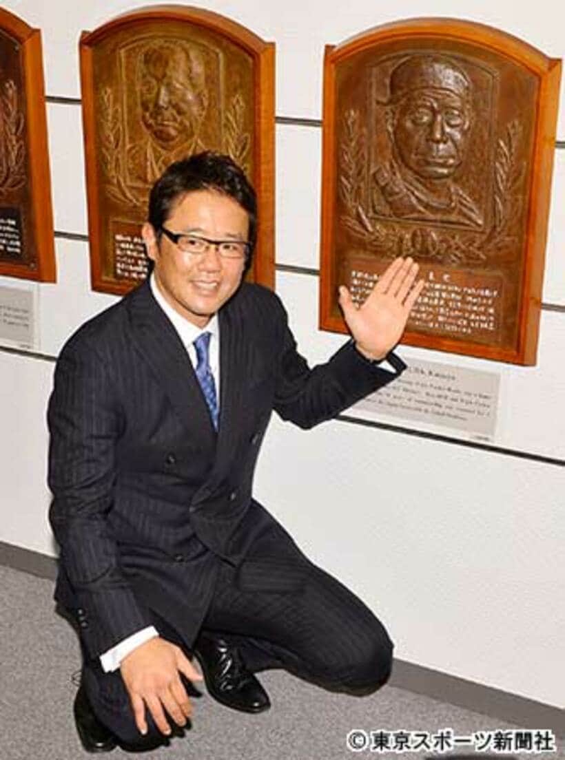 野村克也氏のレリーフの前でポーズをとる古田氏