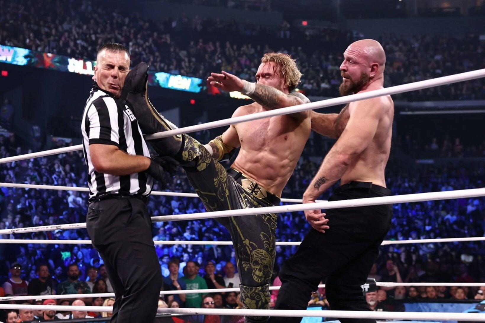 ウィル・オスプレイ（中）のキックがジョン・モクスリー（右）にかわされレフェリーに誤爆（©All Elite Wrestling）