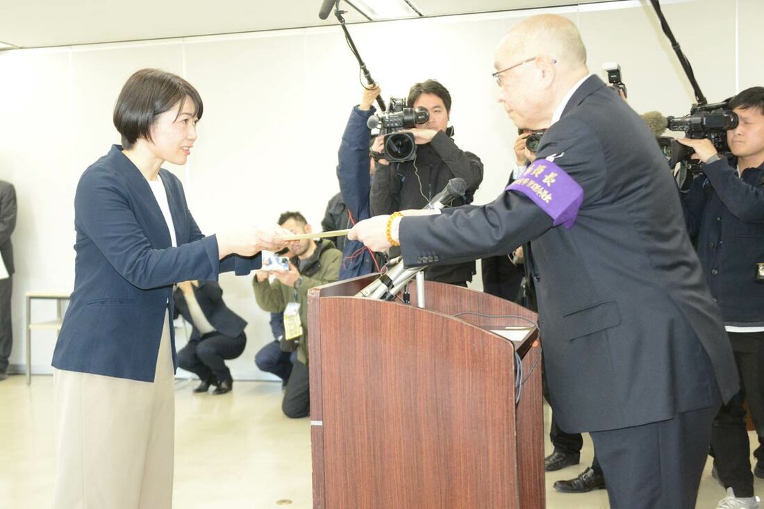 上目遣いで当選証書を受け取る小川晶氏