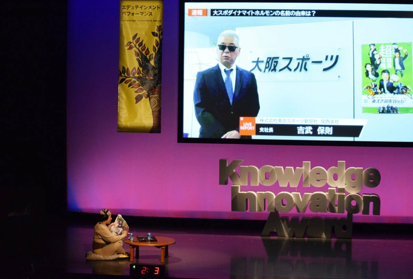 動画プレゼンする吉武支社長(画面)と、それを眺めるオヤジ(左下)