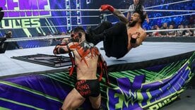 〝ザ・デーモン〟フィン・ベイラー(左)にエプロン上のドロップキックを放つローマン・レインズ(©2021 WWE, Inc. All Rights Reserved.)