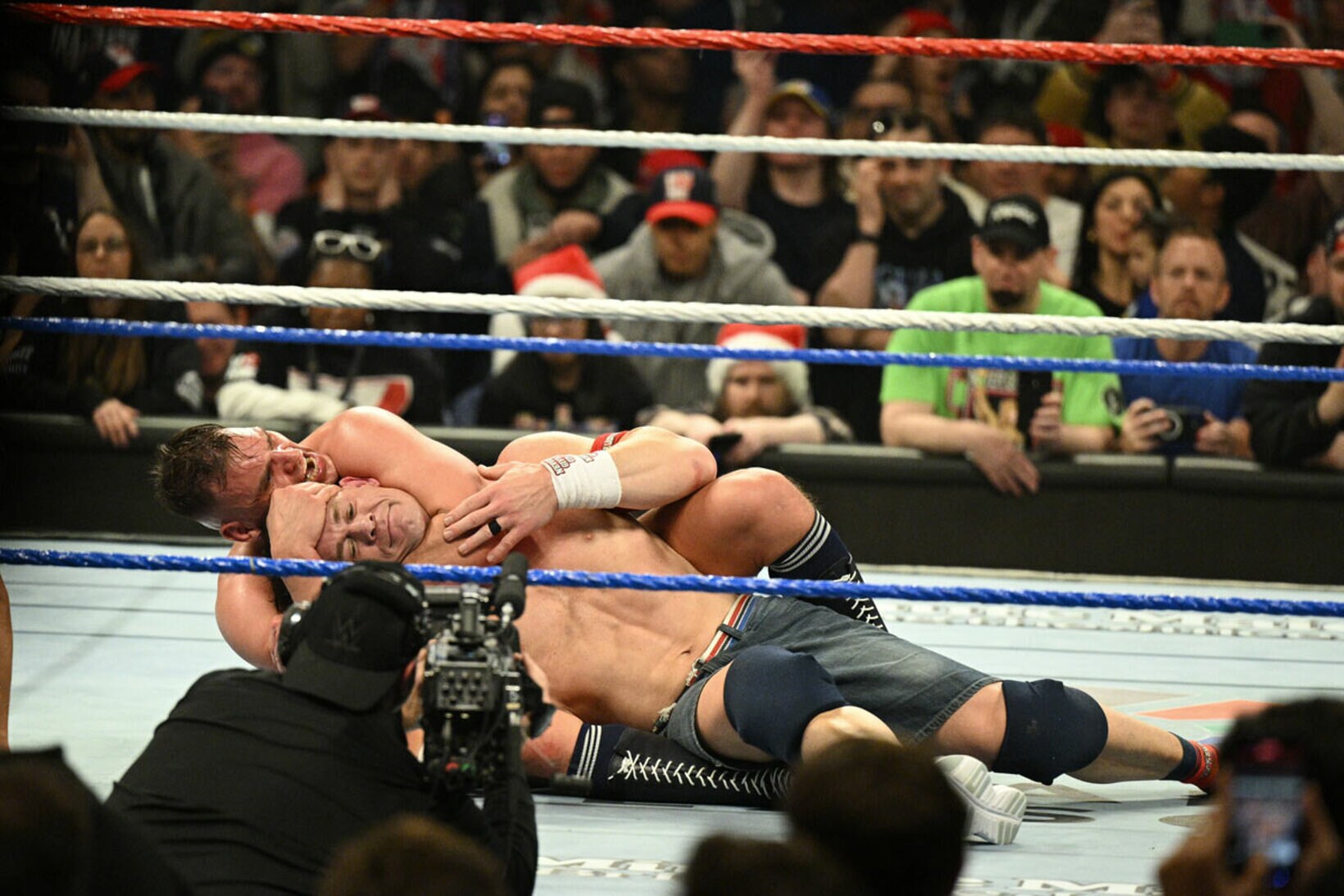 グンター（奥）に胴締めスリーパーで捕獲されたジョン・シナは、笑みを浮かべてタップアウト©WWE