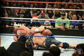 グンター（奥）に胴締めスリーパーで捕獲されたジョン・シナは、笑みを浮かべてタップアウト©WWE