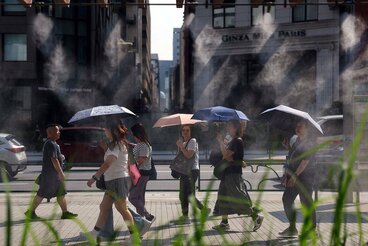 各地で熱中症警戒アラートを発令された２２日、日傘を差し冷却ミストの近くを歩く人々（ロイター）