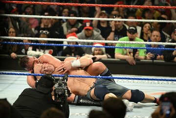 グンター（奥）に胴締めスリーパーで捕獲されたジョン・シナは、笑みを浮かべてタップアウト（©ＷＷＥ）