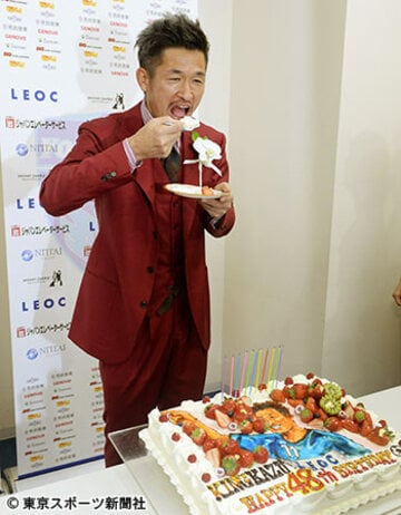 赤いスーツ姿でケーキをパクつくカズ