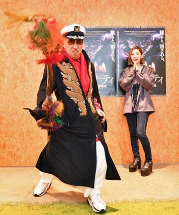  映画のポスターを背にポーズを決める朝堂院氏（左）に目を見張った小島
