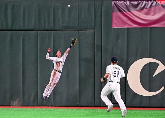 ９回、この大飛球をジャンピングキャッチした侍ジャパン・周東佑京(左)