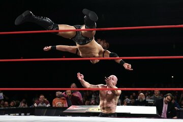 ジョン・モクスリー（下）にノータッチ式トペ・コンヒーロを発射する竹下幸之介©All　Elite　Wrestling