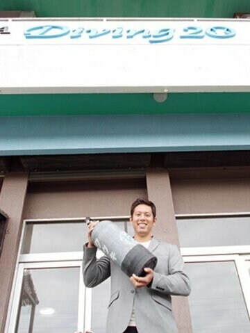  自身の店の前でボンベを手に笑顔の糸数さん