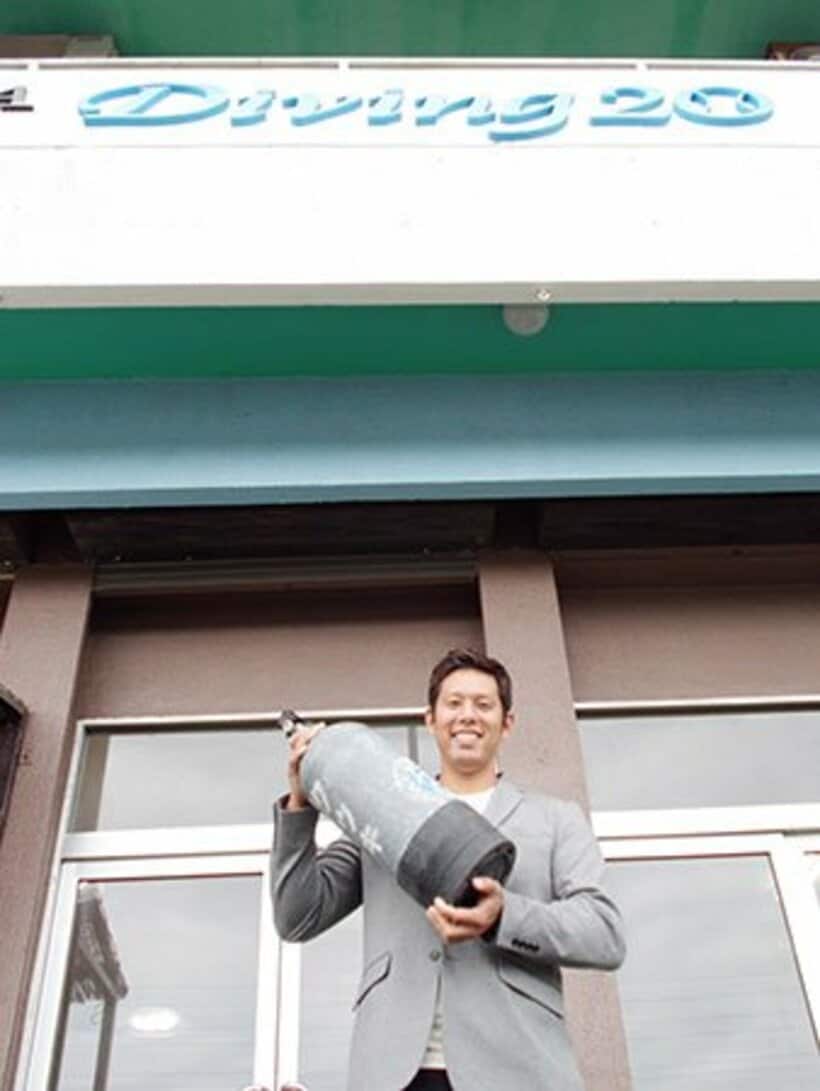 自身の店の前でボンベを手に笑顔の糸数さん
