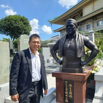 「燃える闘魂　アントニオ猪木之像」の隣で笑顔の小川直也氏