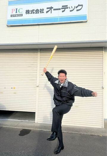 オーテック社屋前でバットを手にポーズを決める真砂さん（提供写真）