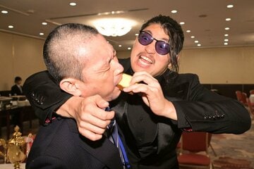 記者の口にカステラを押し込むOZAWA（右）