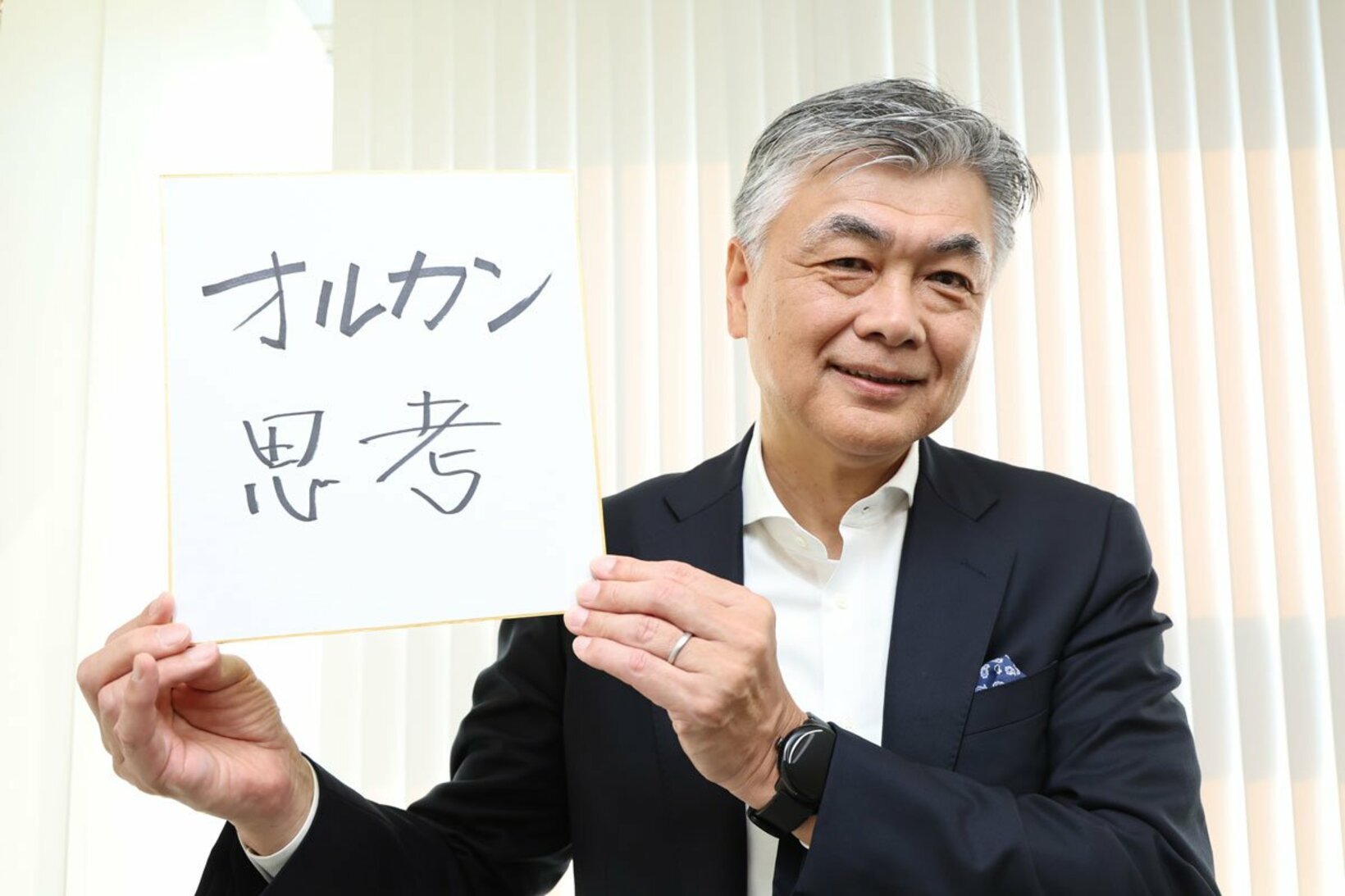 「オルカン思考」と書いた色紙を掲げる代田秀雄氏