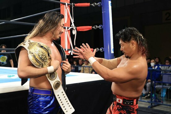 辻陽太(左)の持つ２本のベルトを「品定め」する鷹木信悟