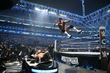 実況席上のローマン・レインズ（下）にCMパンクはエルボードロップ（©WWE）